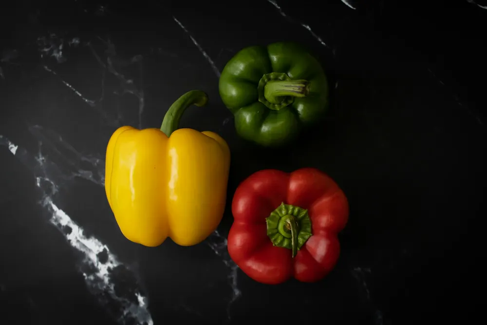 Red, yellow and green capsicums on a dark marble bench